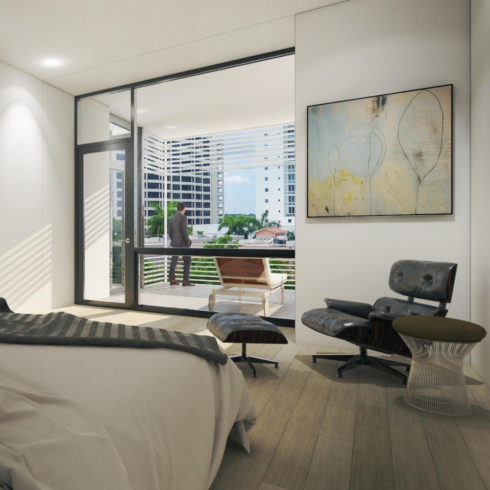 Modern bedroom with a bed, lounge chair, and abstract art. Large glass doors open to a balcony where a person stands, overlooking city buildings and trees.