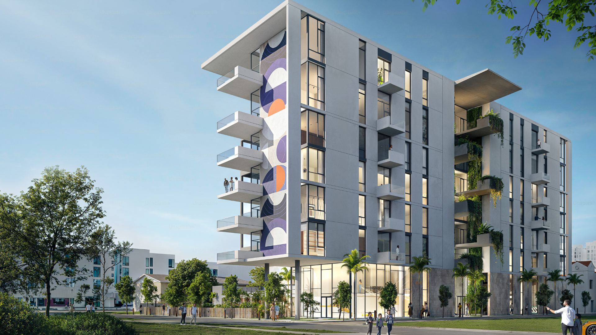 Modern multi-story apartment building with large balconies, geometric wall art, glass windows, palm trees, and people walking outside on a sunny day. The sky is clear, and greenery surrounds the structure.
