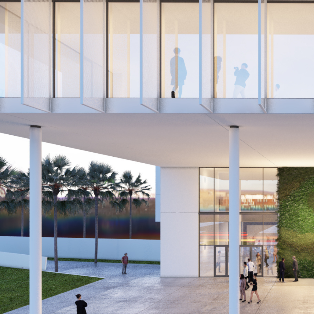 Modern building with glass walls, people walking outside and inside, tall white columns, green wall, and palm trees in the background at sunset.
