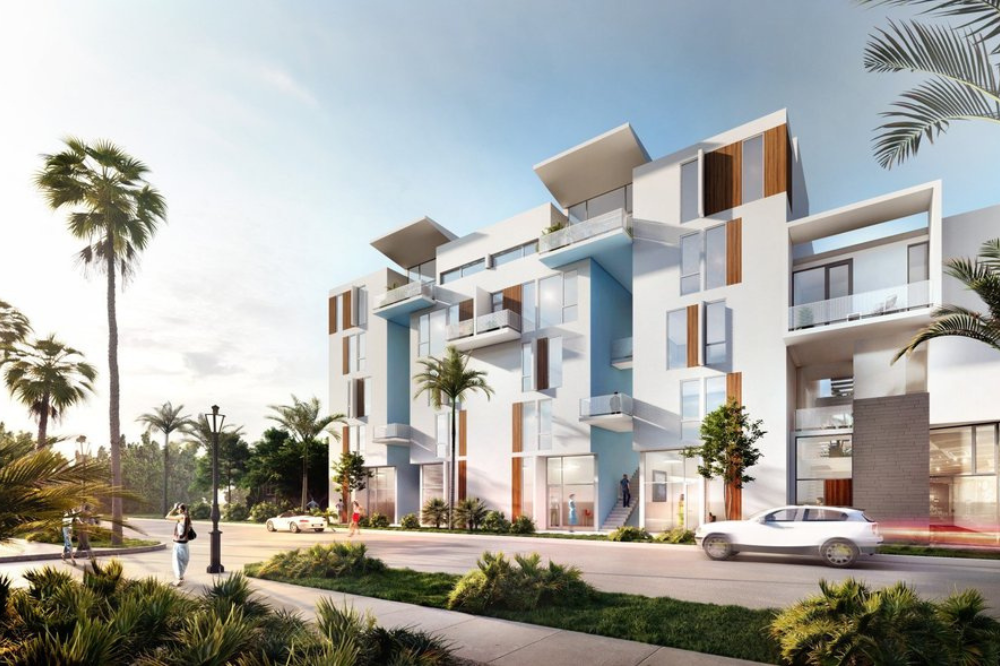 Modern white apartment building with balconies and large windows, surrounded by palm trees and greenery. This award-winning residence sits in a sunny suburb, where people stroll and a white car passes by.