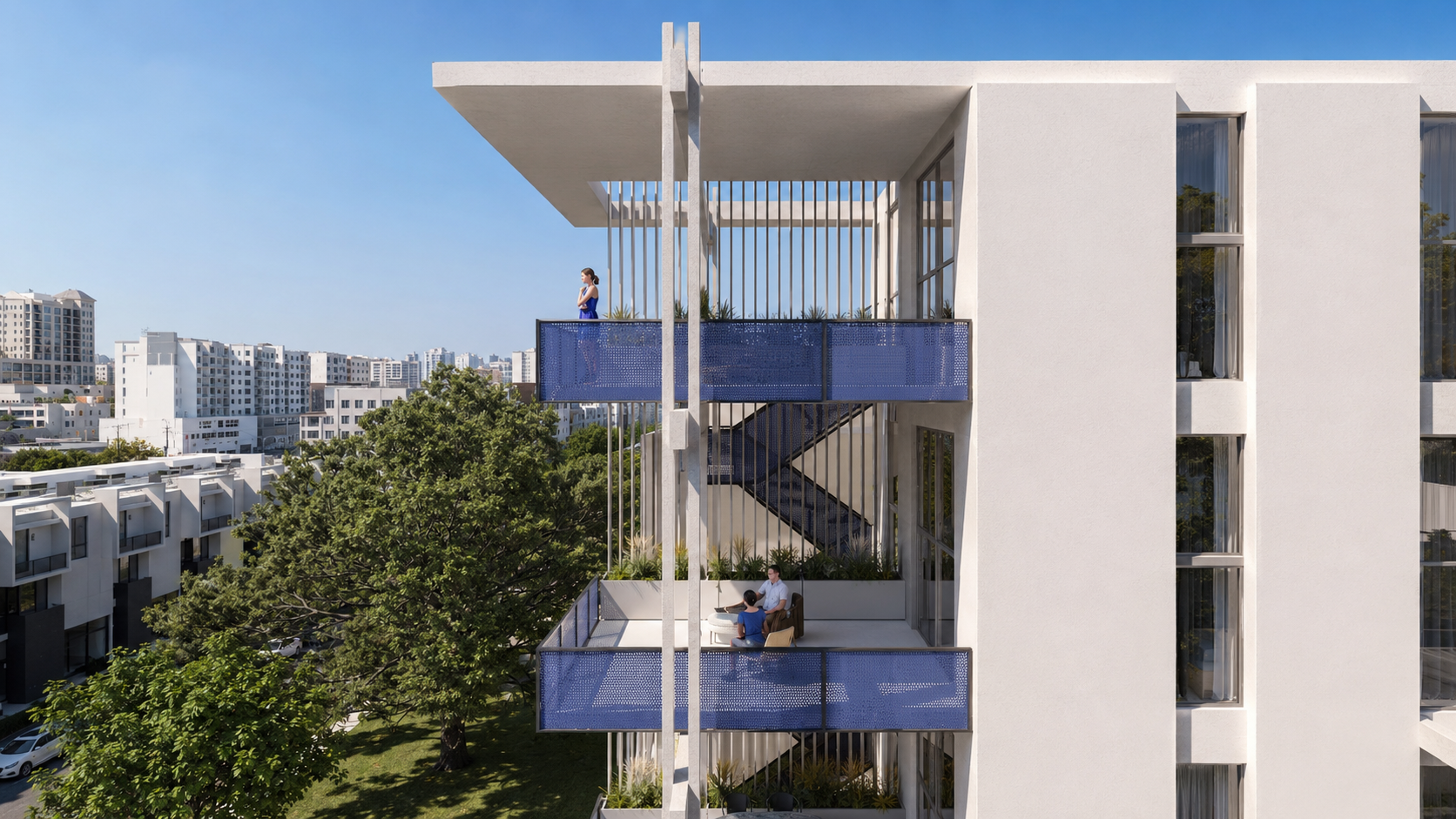 Modern white apartment building with blue-railed balconies; a woman stands on the upper balcony and two people sit on the lower balcony. Trees and other buildings are visible in the background under a clear sky.