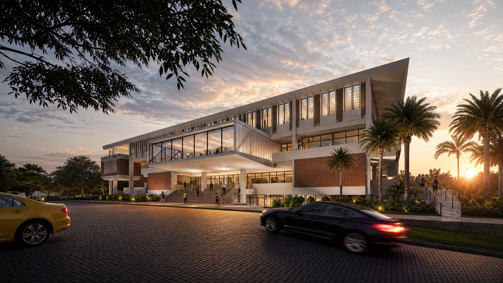 A modern building with large windows, surrounded by palm trees at sunset. Cars drive by on a brick road while people walk up the stairs to the entrance. The sky is partly cloudy with warm light.
