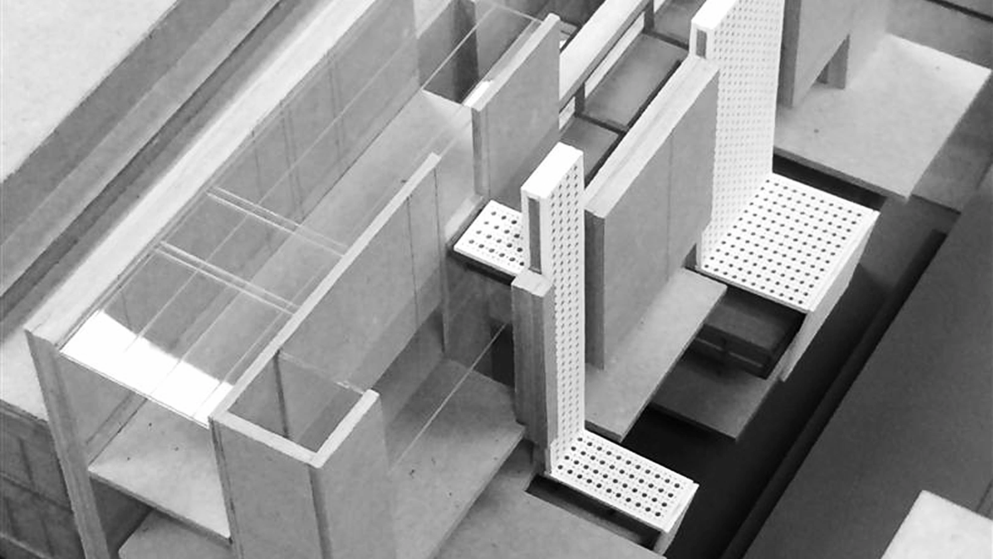 A black and white photo of an architectural model at USF, featuring geometric structures, transparent panels, and perforated white surfaces representing building elements.