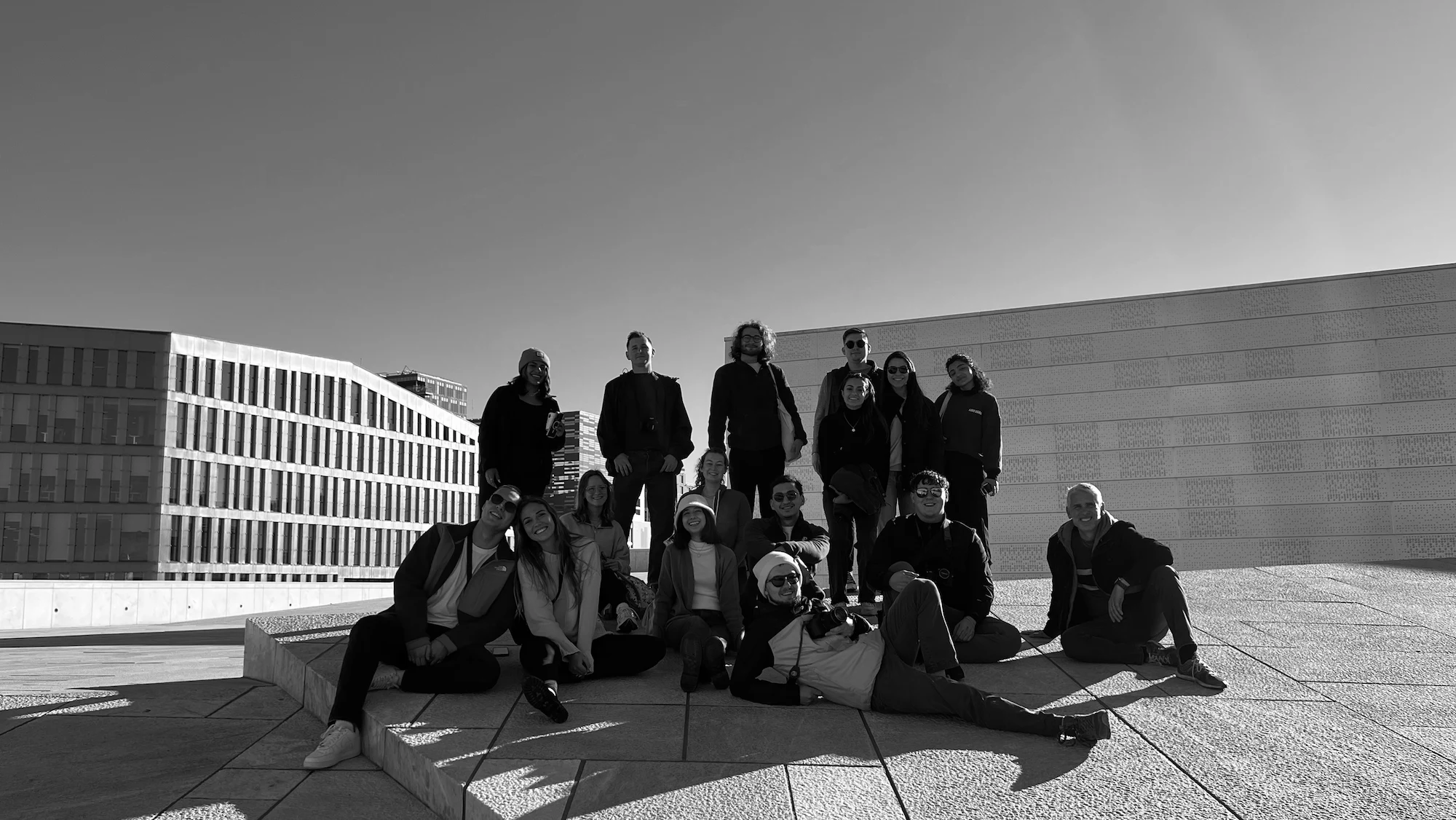 A group of people pose together on a modern, angular outdoor structure at USF, with minimalist buildings in the background under a clear sky.